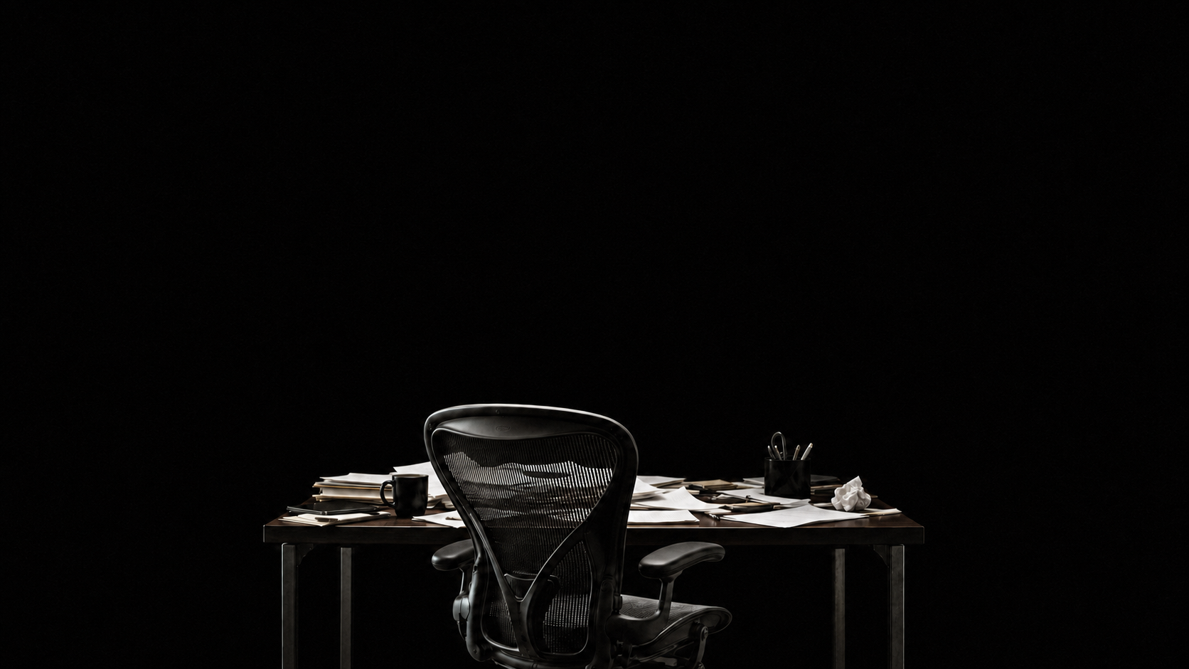 An empty office chair behind a work table covered in paperwork
